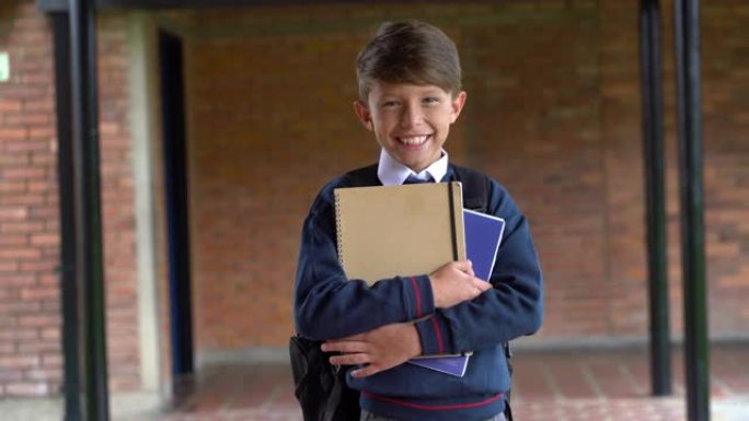 开朗的小男孩拿着笔记本穿着校服对着镜头微笑