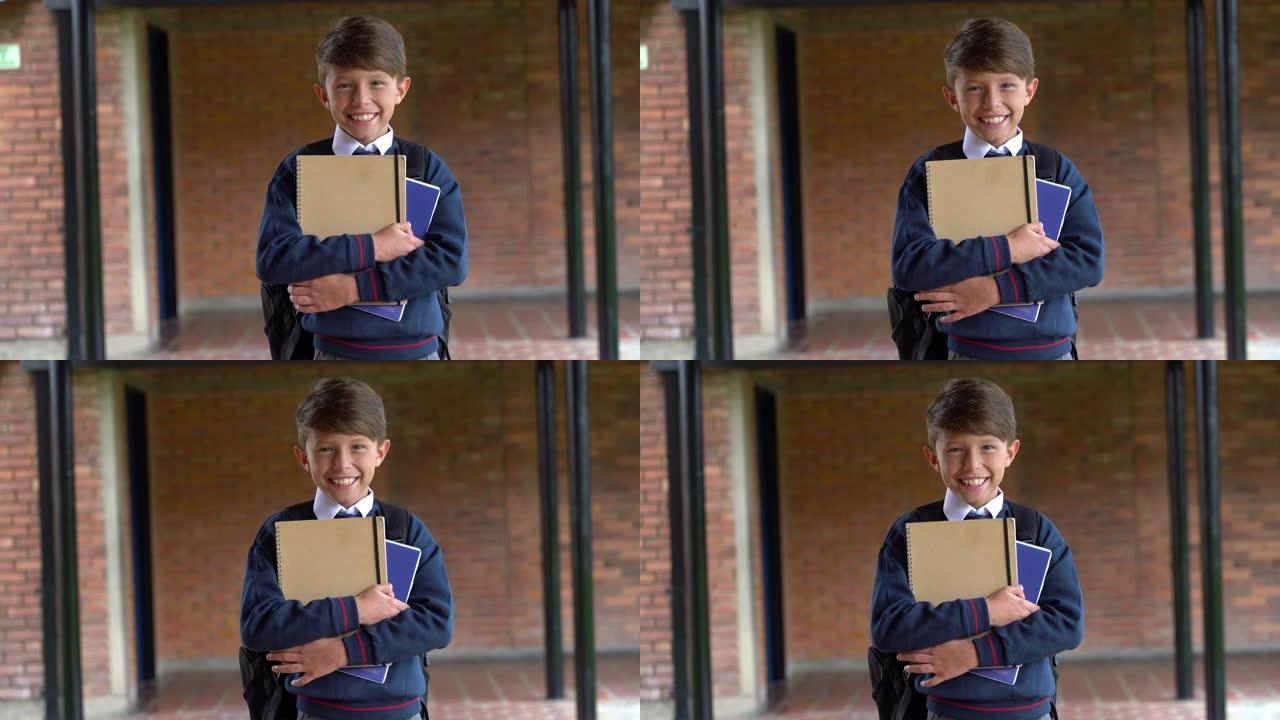 开朗的小男孩拿着笔记本穿着校服对着镜头微笑