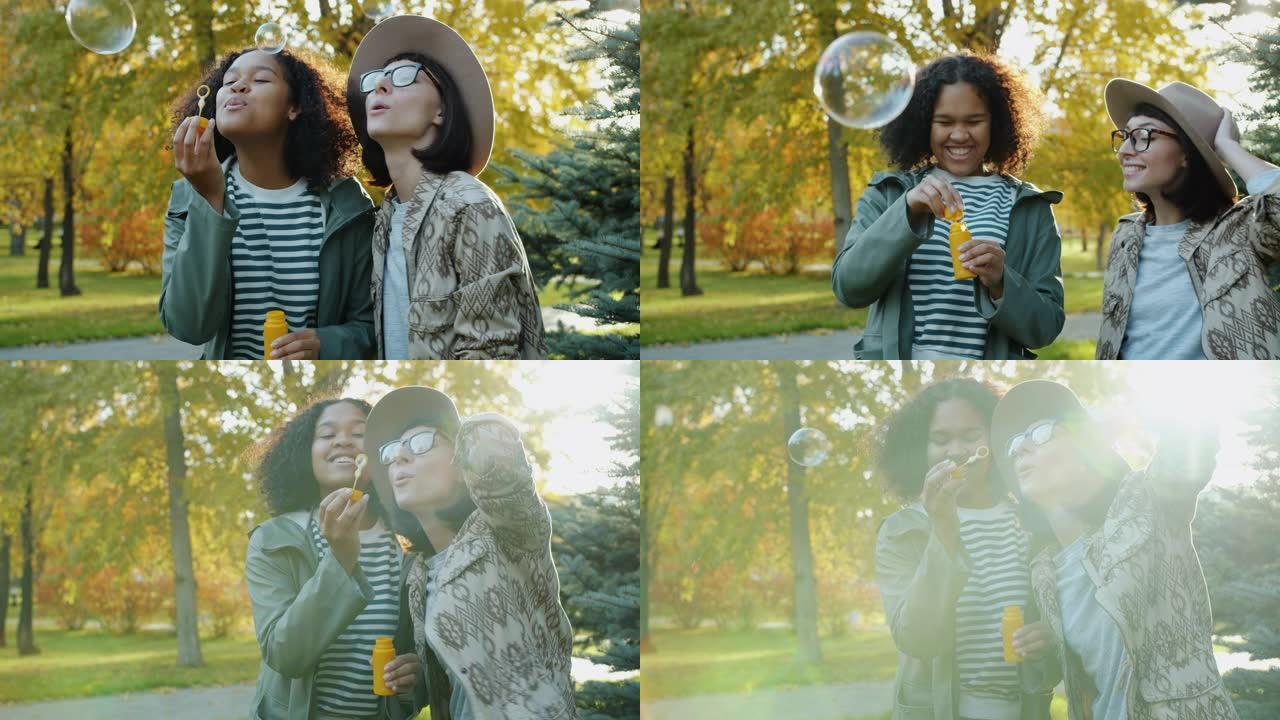 快乐的年轻女性朋友在阳光明媚的秋天在公园吹肥皂泡