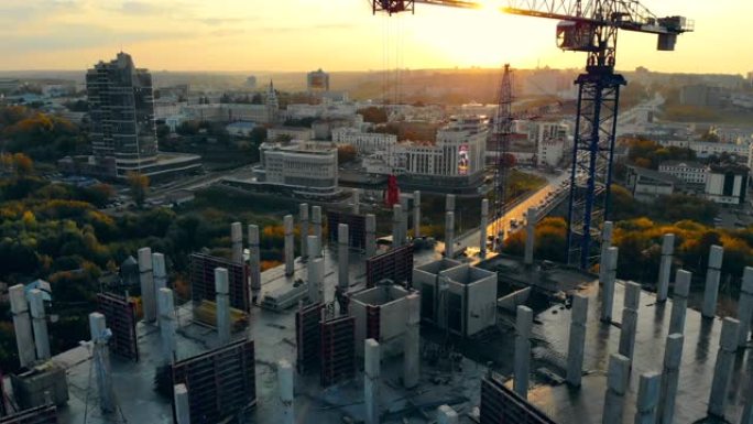 高层建筑正在进行中，配有日落时的机械。日落时的现代建筑工地，鸟瞰图。