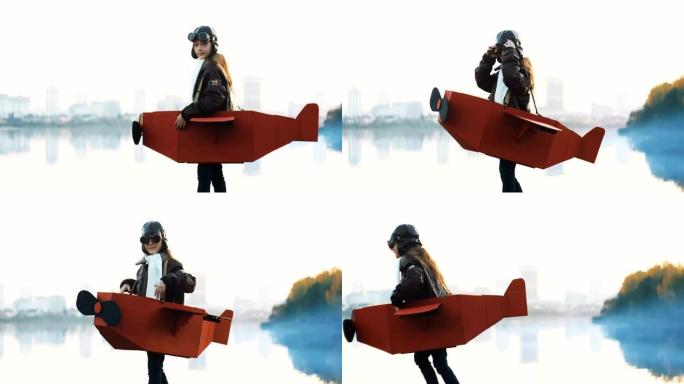 小飞行员女孩在大城市湖上的纸板飞机上扮演飞行员，回头看，戴着旧眼镜慢动作。
