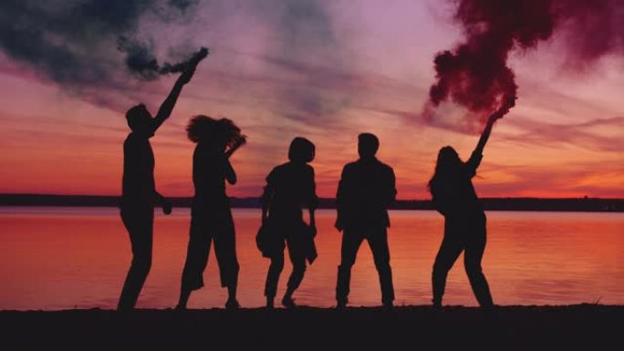 日落时分，快乐的朋友在湖边跳舞，手持烟雾弹聚会