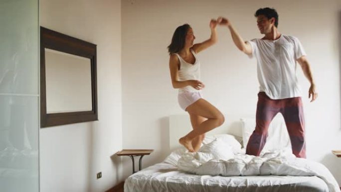 穿着睡衣的年轻新婚夫妇的慢动作在阳光明媚的清晨在卧室里跳舞