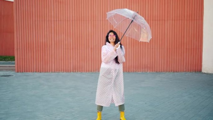 穿着雨衣和橡胶靴的亚洲女人的慢动作与雨伞跳舞