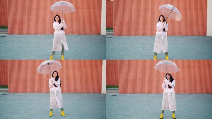 穿着雨衣和橡胶靴的亚洲女人的慢动作与雨伞跳舞