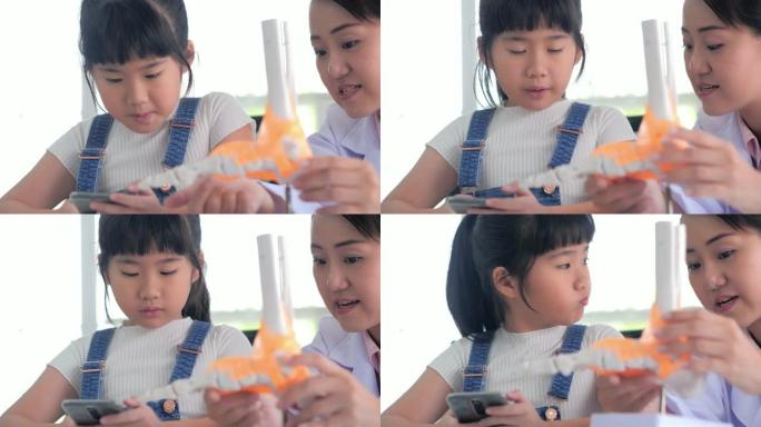 可爱的年轻女孩使用智能手机并触摸骨骼，同时试图与老师一起检查它是否真实。教育主题。