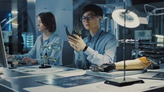 未来的假肢机器人手臂由专业的日本开发工程师在高科技研究实验室中使用现代设备进行测试。他的同事正在电脑