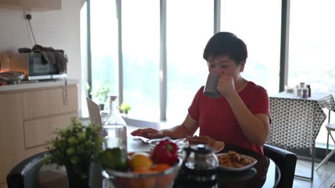 一位亚洲华人中年人在餐厅吃早餐，早上用笔记本电脑回复电子邮件