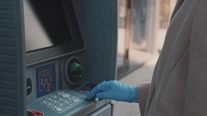 女人用防护手套从自动取款机取钱。冠状病毒大流行