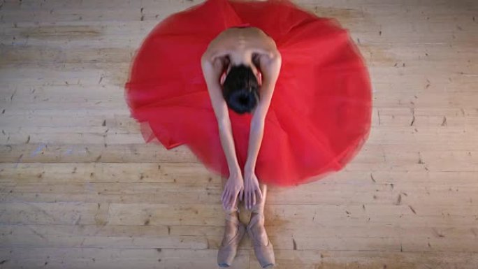 一位美丽的轻型芭蕾舞演员的肖像，穿着一件郁郁葱葱的红色连衣裙，坐在木地板上，灵活，俯视图。