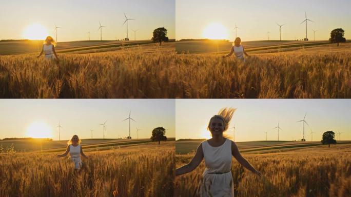快乐的女人一边抚摸着小麦，一边跑在远处有风力涡轮机的田地里