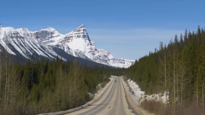 POV: 沿着空旷的道路行驶，可以看到白雪皑皑的加拿大落基山脉