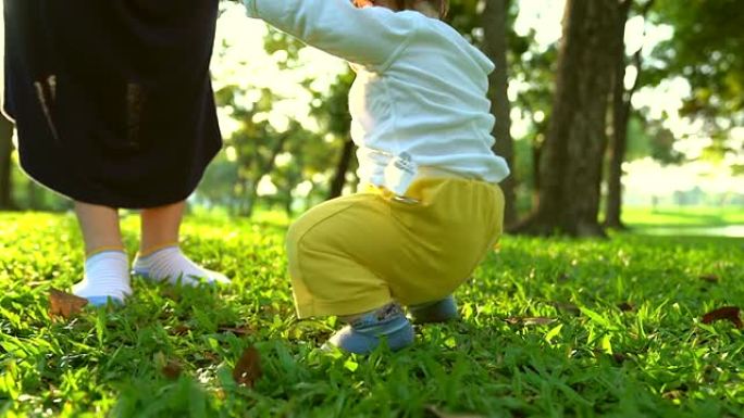 母亲教婴儿在草地上学习第一步。第一个独立的步骤。