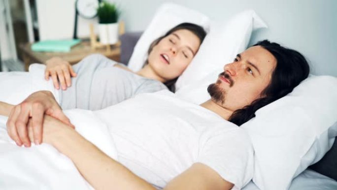 不幸的男人丈夫用枕头遮住头，而妻子在床上打鼾