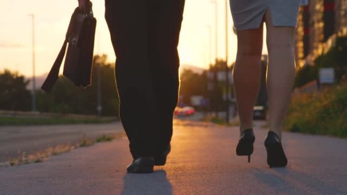 穿着高跟鞋的镜头耀斑女孩和她的同事在日落时走在人行道上
