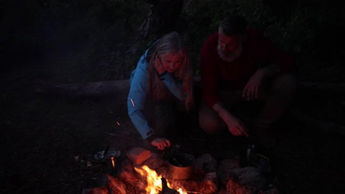 白人高级夫妇在篝火旁在营地准备饭菜