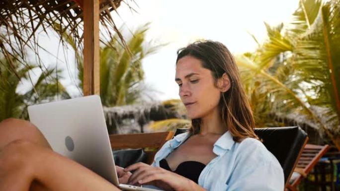 美丽的高加索工作狂首席执行官女商人工作，度假时在沙滩椅上的笔记本电脑移动办公室打字。
