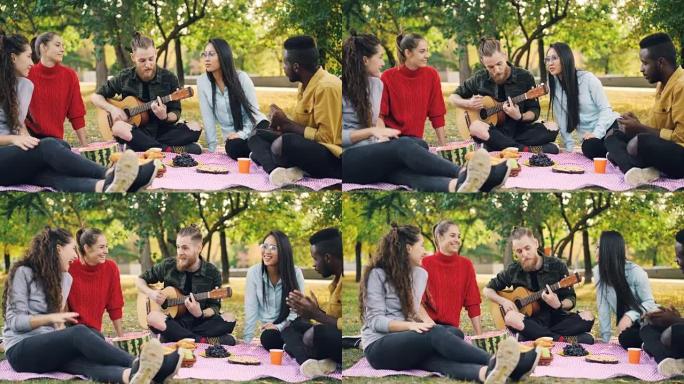 帅哥在弹吉他，而他的男女朋友在公园听音乐、唱歌和野餐时玩得开心。友谊和文化理念。