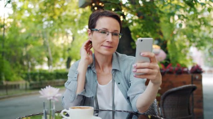 漂亮的女士独自在户外咖啡馆用智能手机自拍放松