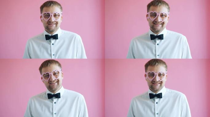 粉色背景上戴着心形眼镜的帅哥在相机前微笑的肖像