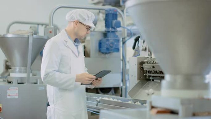 年轻的男性质量主管或食品技术员正在饺子食品工厂检查自动化生产。员工使用平板电脑工作。他戴着白色的卫生