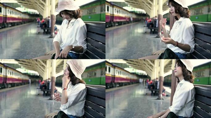 快乐的亚洲青少年妇女戴着耳机听音乐，夏天在火车站等候。泰国旅游概念。