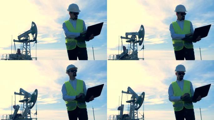 工程师用笔记本电脑工作，站在一个有油井架的油田上。