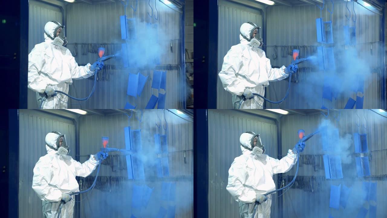 一名工人正在油漆工厂的金属件上喷涂蓝色油漆