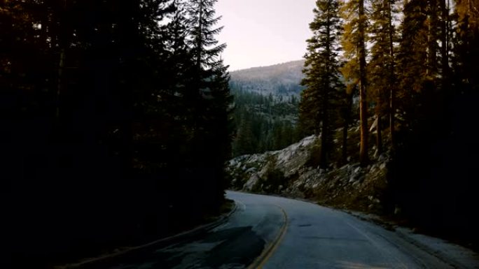 在约塞米蒂慢动作中，车辆上的摄像机正沿着美丽的森林山路在日落时分在树木之间转弯。