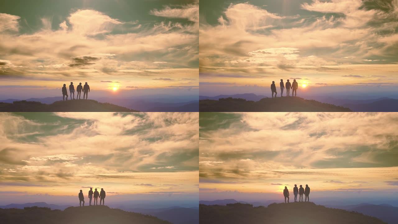 四个人站在美丽的日出背景上的山上