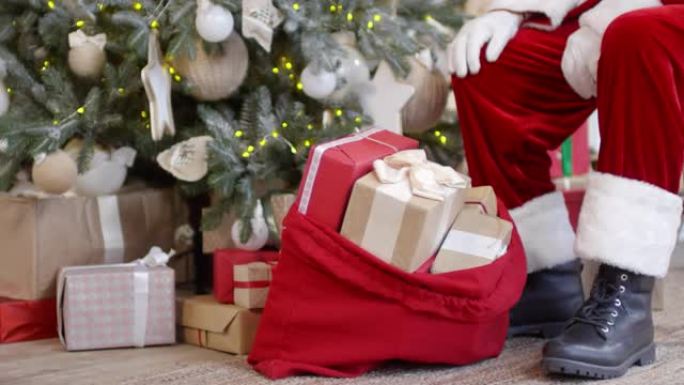 圣诞老人坐在圣诞树和带礼物的袋子附近