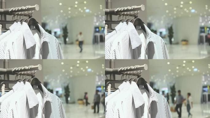 4k镜头在衣架上悬挂衣架和栏杆的场景以及在百货商店，购物中心和服装概念的时尚服装店购物的人们