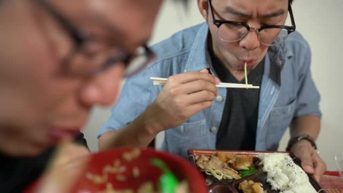 两名亚洲男子吃日本料理中常见的便当、单份外卖或家庭包装餐。
