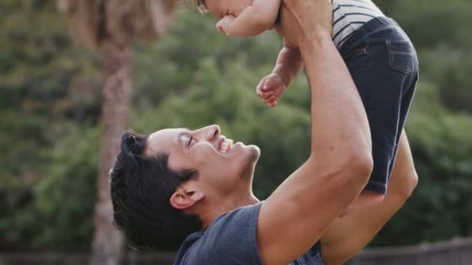 千禧一代西班牙裔男子在公园的空中举起他的小儿子，特写镜头