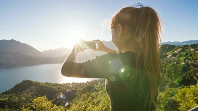 女游客拍摄意大利科莫湖和湖边村庄的全景照片，背景是欧洲阿尔卑斯山