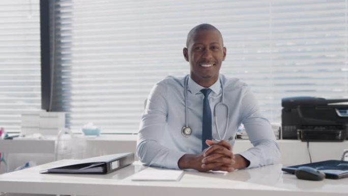 微笑的男医生坐在办公室桌子后面的肖像