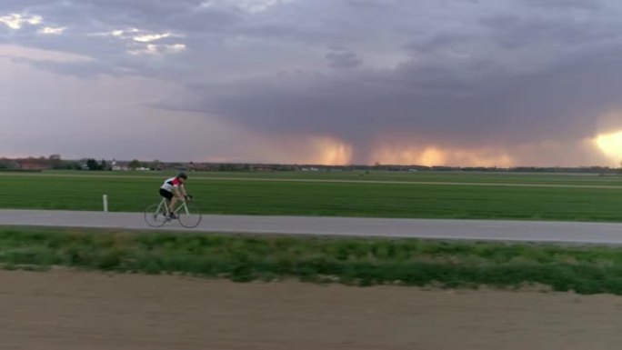WS男骑自行车者在乡村道路上骑自行车，背景为暴风云