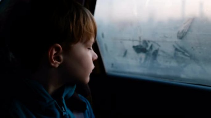 3-6岁可爱的悲伤的高加索男孩在黑暗的夜晚骑行中从雾蒙蒙的车窗向外看的电影镜头。
