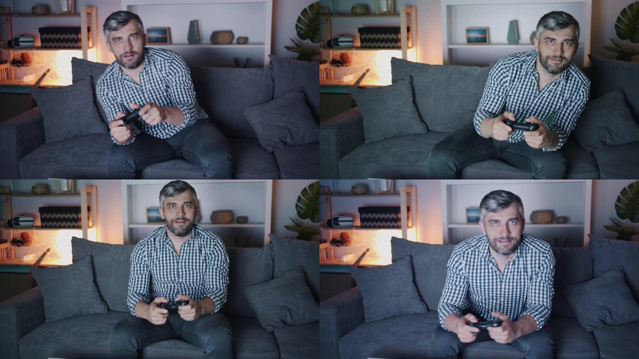 快乐男人玩电子游戏的肖像晚上在家看着相机