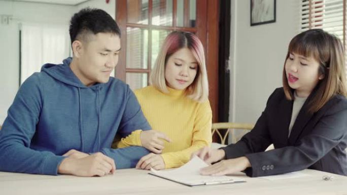 快乐的年轻亚洲夫妇和房地产经纪人。开朗的年轻人和妻子一起坐在办公桌前签署一些文件。购买新房房地产。签