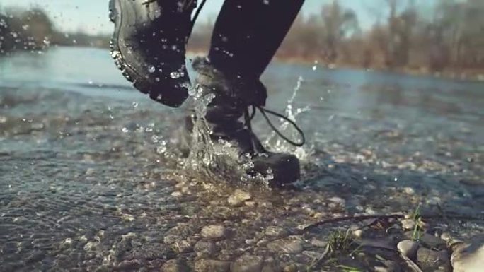 慢动作: 穿着黑色防水靴的女孩溅起清澈的湖水。