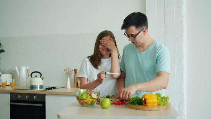 男人丈夫在厨房做饭时快乐的女孩带怀孕测试