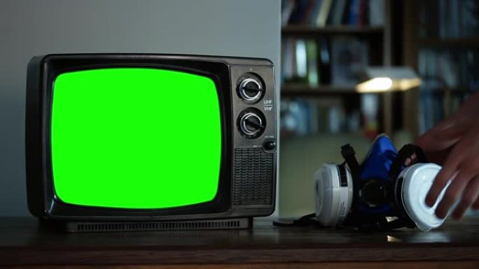 手拿起面部呼吸器面罩和带有绿色屏幕的复古电视。特写。您可以在After Effects中使用 “键控