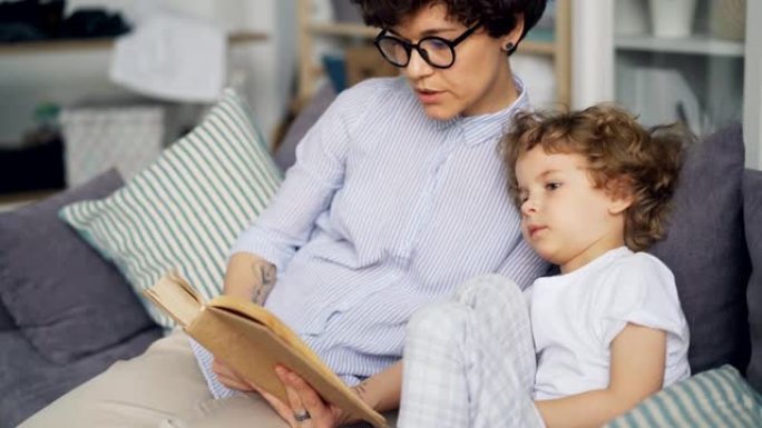 有爱心的妈妈给坐在房间沙发上的小孩读书可爱的卷发男孩