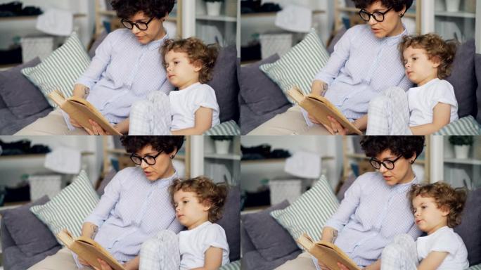 有爱心的妈妈给坐在房间沙发上的小孩读书可爱的卷发男孩