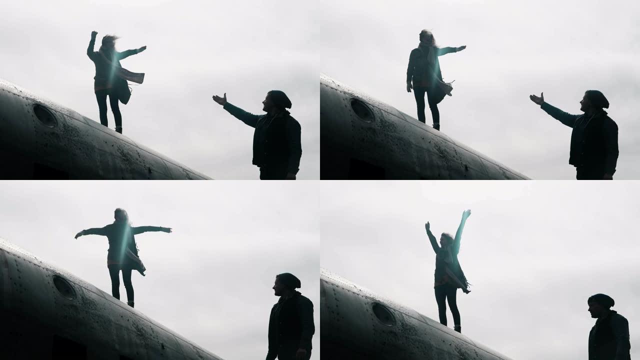 年轻女子站在冰岛坠毁的DC-3飞机的顶部，伸出手向站在附近的男子伸出手。