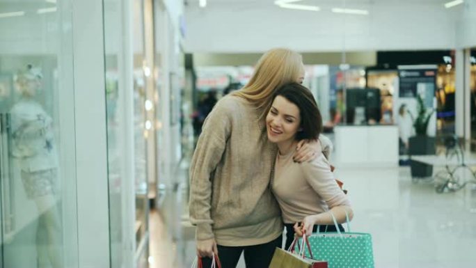 快乐的年轻女性朋友在购物中心开会，讨论购买商品，并在纸袋中查看商品，然后一起购物。友谊和购物狂的概念