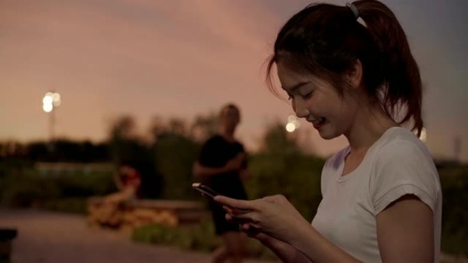 开朗的亚洲旅游博客写手女人在夜间在市区的街道上行走时，在智能手机上使用触摸屏技术。生活方式背包旅游度