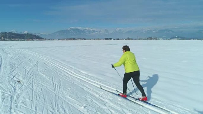 空中: 穿着五颜六色的夹克沿着女人在雪地里的小径滑雪。