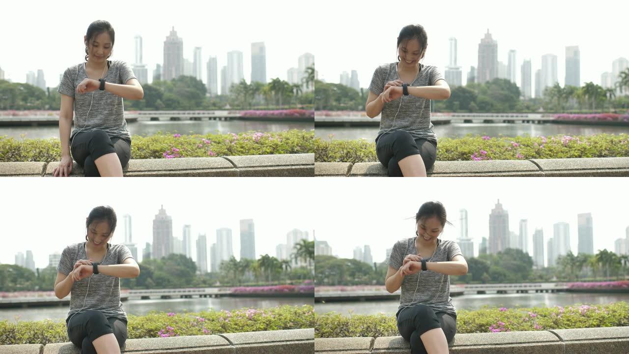一个穿着耳机的漂亮健身女人的肖像在城市户外检查她的智能手表